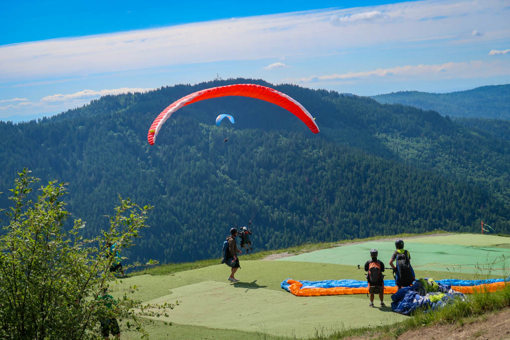A group of paragliders stand on Poo Poo Point on Tiger Mountain, with one of them jumping off