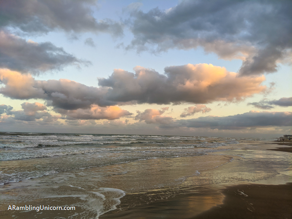 Moody clouds reflect light from the sunset in the water at the beach on South Padre Island