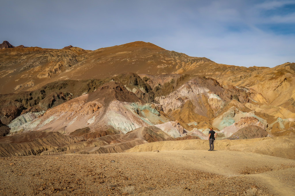 Daniel stands in front of Artists Palette - brown hillside splashed with a range of colors including pink, blue, green and orange.