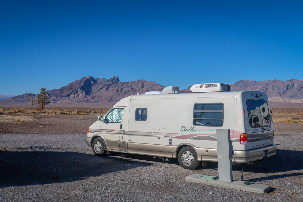 Our Rialta motorhome is parked in a RV resort parking lot with views of the desert mountains in the distance
