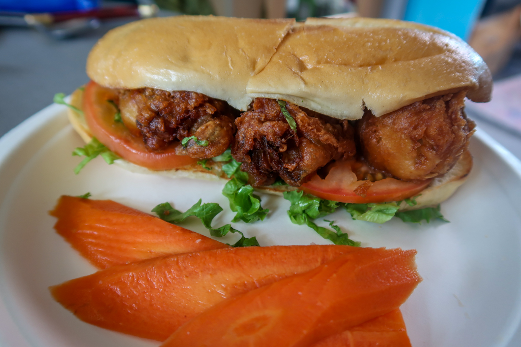 Oyster po boy sandwich with three large fried oysters, lettuce and tomato, on a plate with pickled carrots