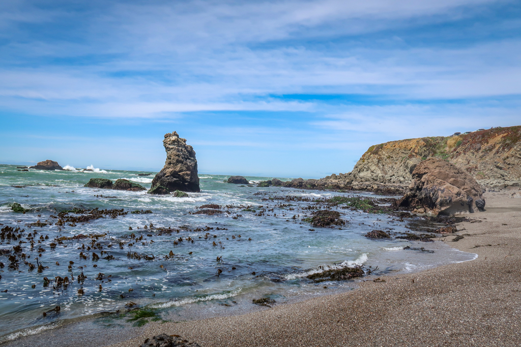 A sandy beach interspersed with rugged rocks and a sea stack poking out of the water