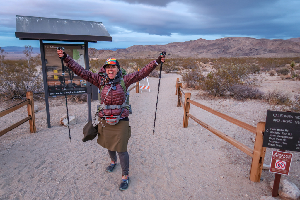 The author poses triumphantly at the North Entrance trailhead with both her hiking poles raised in the air.