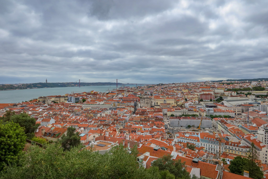 View of the city of Lisbon with many terra cotta tile roofs and the 25 de Abril Suspension Bridge in the distance