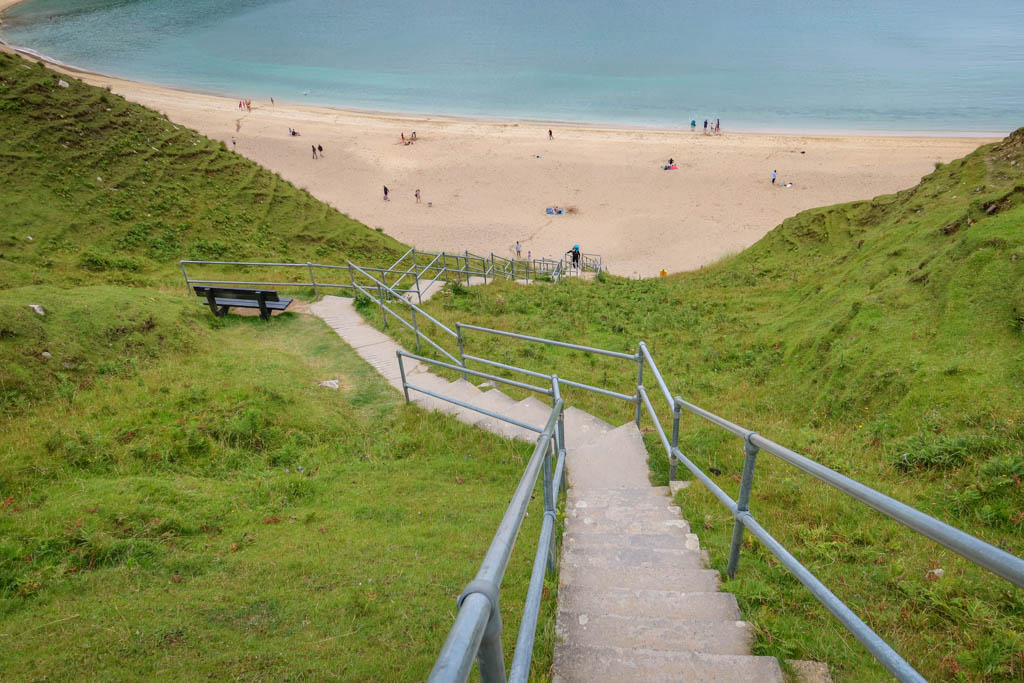 A long series of steps leads steeply downhill to a sandy beach in a hidden cove