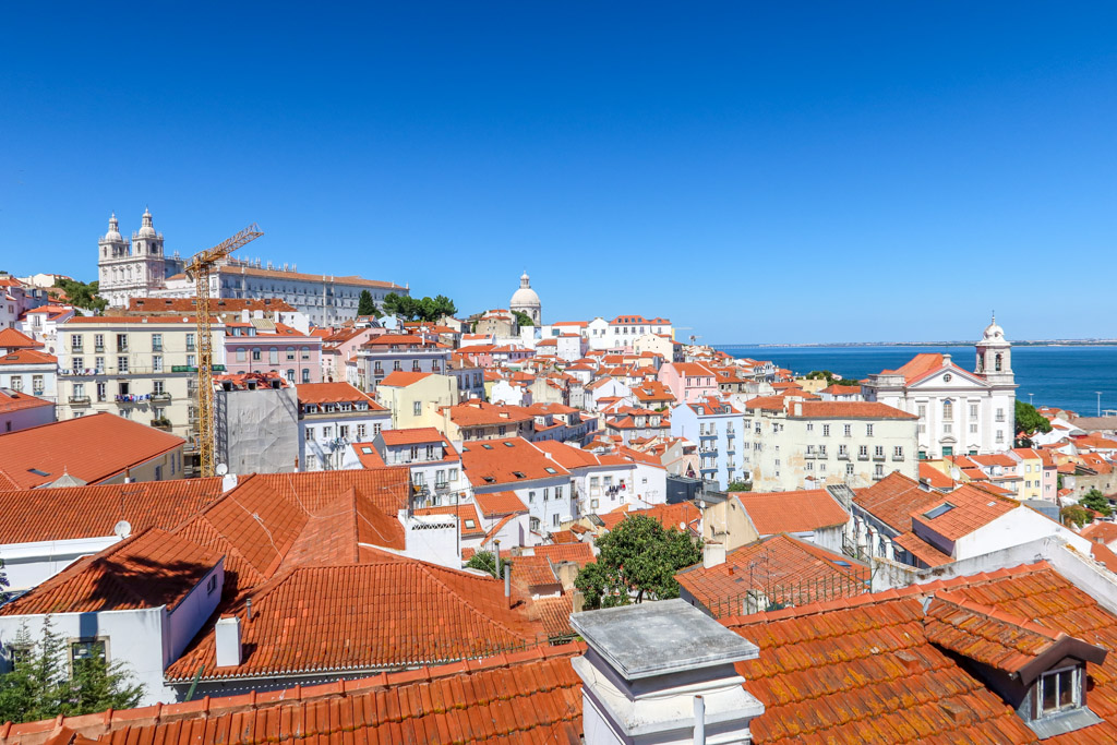View of red-tiled roofs in Lisbon's Alfalma neighborhood and the Tagus River in the distance