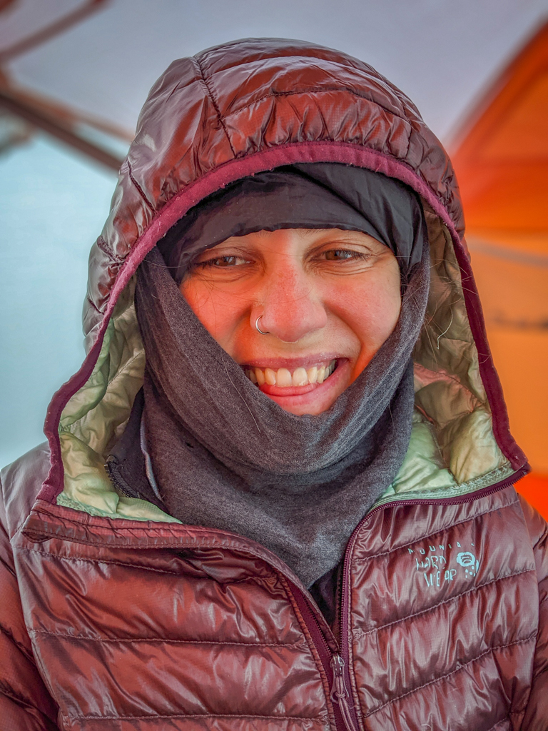 Photo of the author bundled up in a puffy jacket and wool neck gaiter along with a down stocking hat and other warm layers of clothing inside the tent.