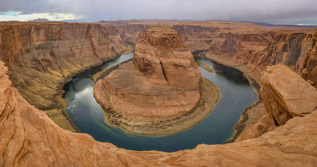 Horseshoe Bend, an enormous U-shaped bend in the Colorado River, surrounded by towering red canyons over 1000 feet tall.
