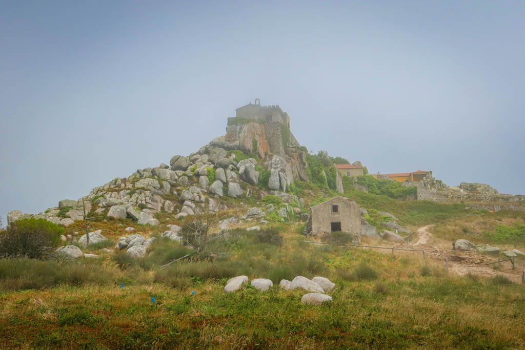 A historic stone church stands on a rocky knoll surrounded by fog