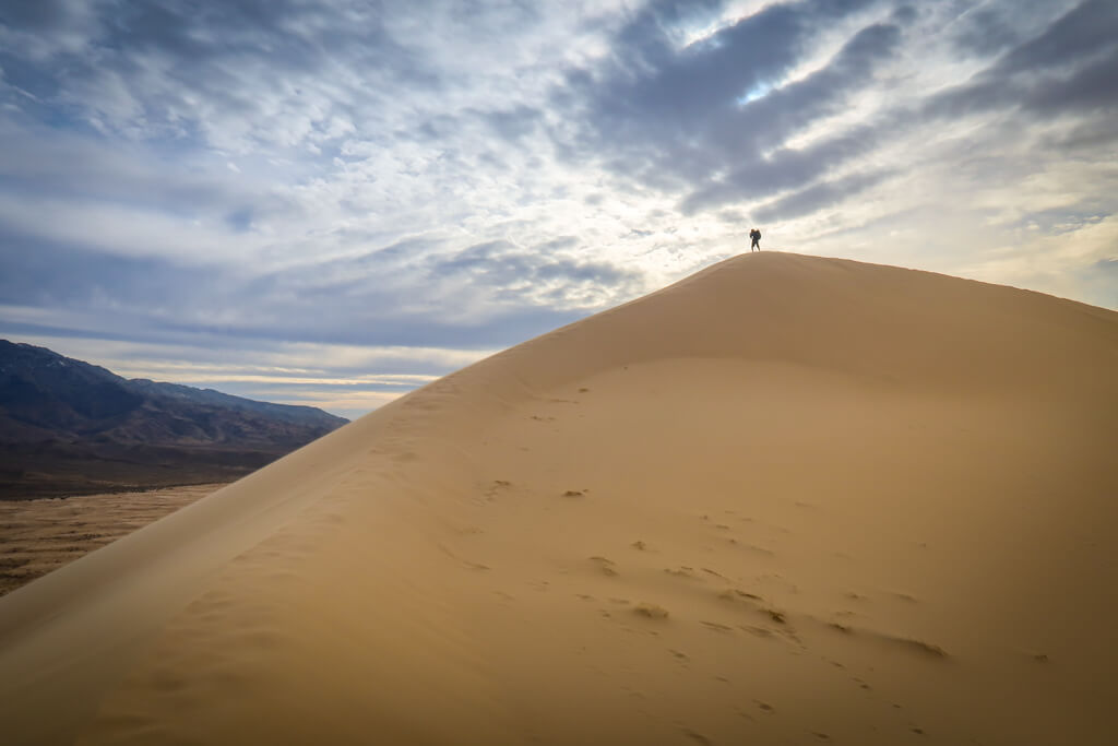 Silhouette of a photographer with a tripod taking a photo at the top of the dunes