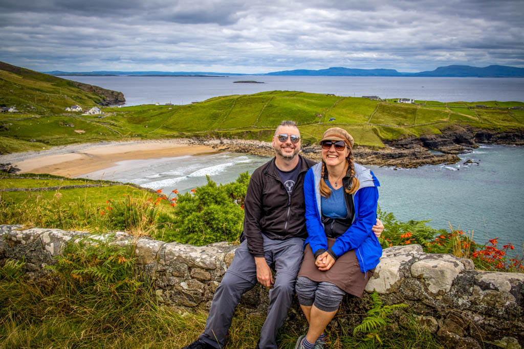 The author and her husband sit on stone wall with Muckross Head in the background on their Donegal day trip