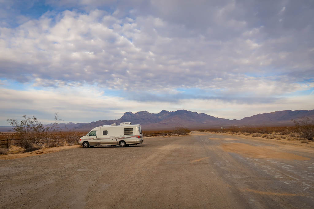 Winnebago Rialta parked near the trailhead for Kelso Dunes with colorful mountains in the distance at Mojave National Preserve