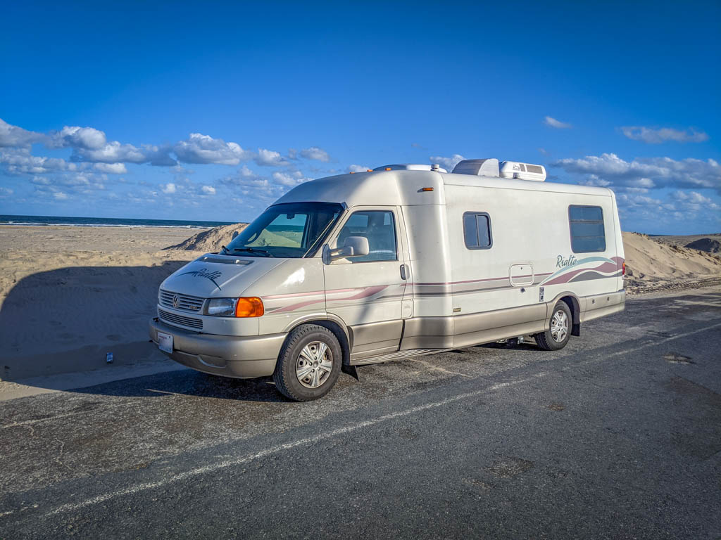 Winnebago Rialta parked along a sandy beach with dunes framing the road on either side in South Padre Island