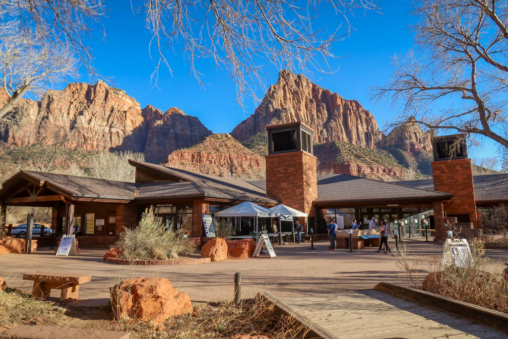 One day in Zion National Park should start at the Zion Visitor Center - the building is framed with the sandstone cliffs of Zion Canyon in the background