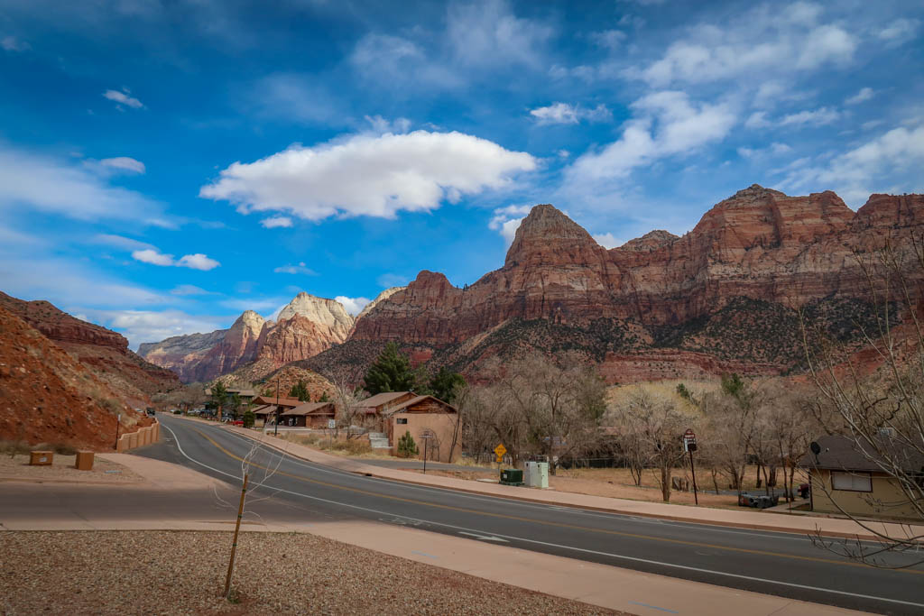 The road leading into Zion National Park with tall jagged red-streaked canyon walls in the background and a blue sky