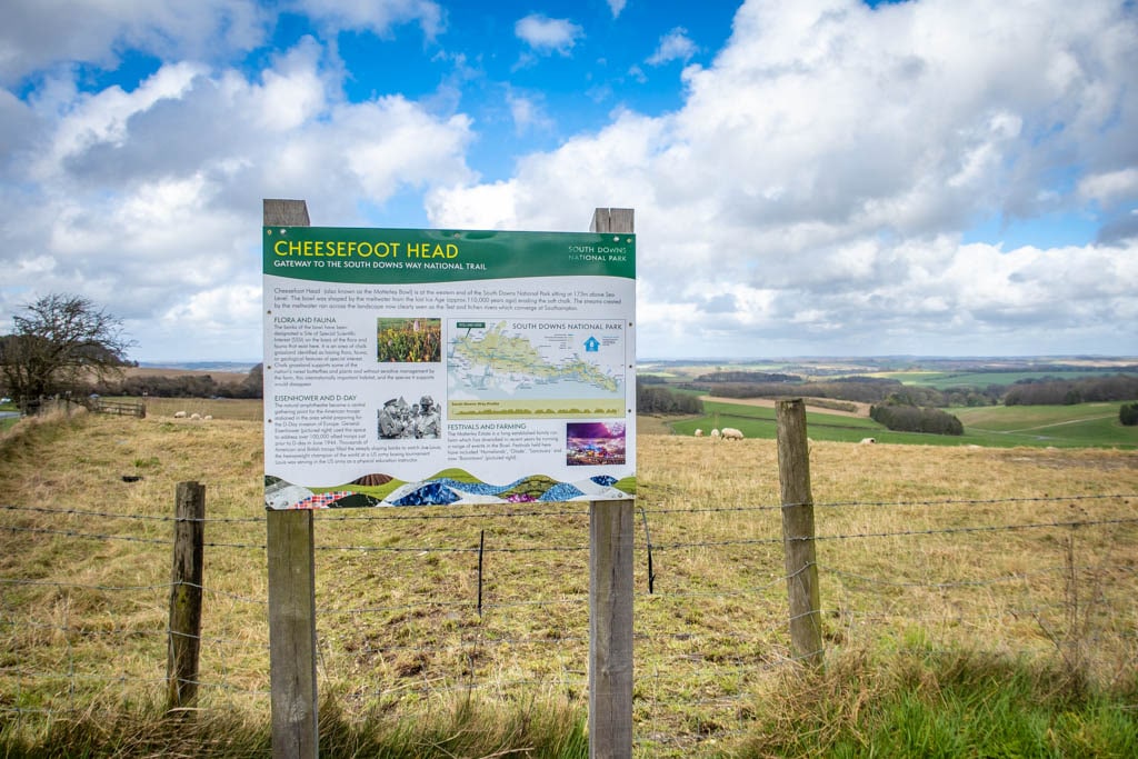 View of Cheesefoot Head with an informational sign containing details about flora and fauna along with historical details about WWII and D-Day and a map of South Downs Way.